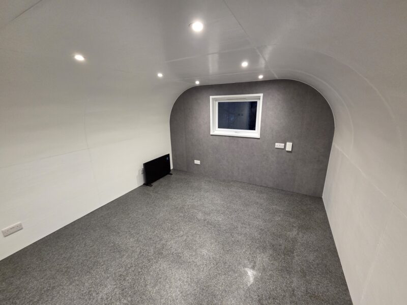 eLodge Max garden lodge interior with ceiling spotlights, upgraded heater, and concrete effect feature wall